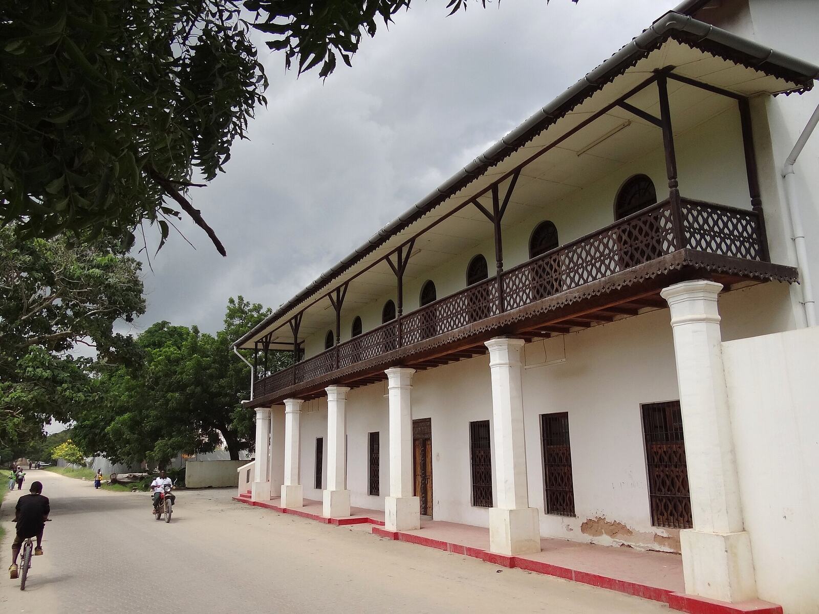 The Old Arab Tea House in Bagamoyo: white walls, a carved wooden balcony, a cyclist passing